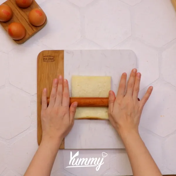 Taruh roti tawar di atas talenan dan pipihkan dengan bantuan rolling pin.