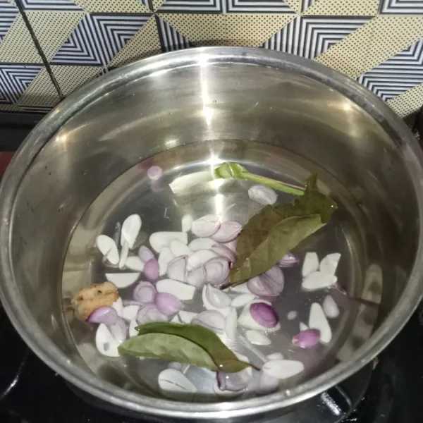 Rebus air, bawang merah, bawang putih, lengkuas,daun salam dan serai di panci.