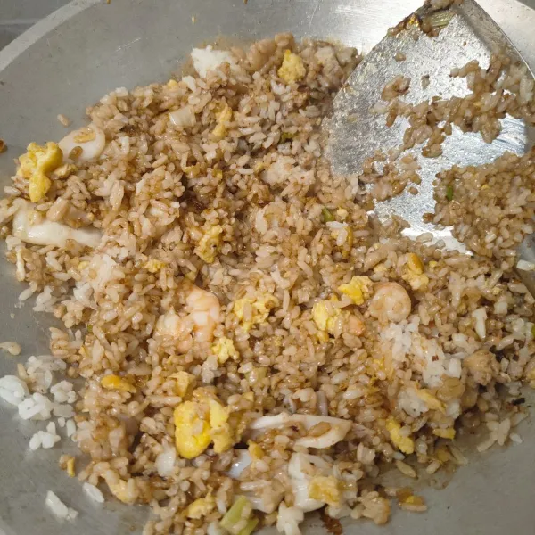 Campurkan juga semua topingnyang sudah di masak, gunakan api besar saat mengaduknya supaya nasi goreng beraroma asap. Sajikan.