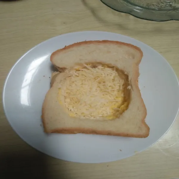 Letakkan roti tawar yang telah dilubangi di atas roti tawar utuh, beri parutan keju.