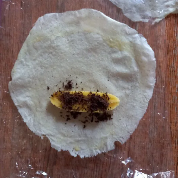 Ambil kulit lumpia, taruh pisang dan taburi cokelat lalu gulung kulit lumpia, beri lem di ujungnya (lem terbuat dari campuran tepung terigu dan air).