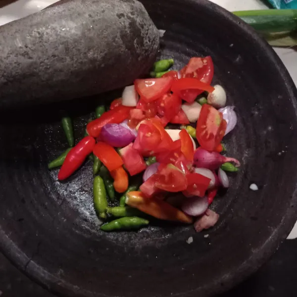 Masukan tomat, cabe rawit ijo, cabe rawit merah, bawang merah, bawang putih ke dalam cobek.