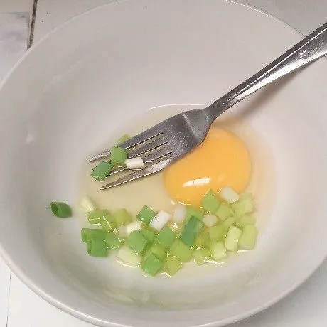 Pecahkan telur di mangkuk. Tambahkan irisan daun bawang.