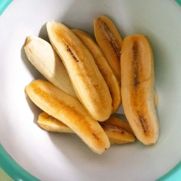 Kupas pisang dan potong menjadi 2 bagian.