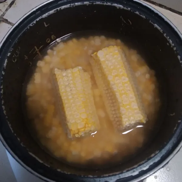 Masukan jagung berserta bonggolnya ke dalam magicom yang berisi beras tadi, lalu tambahkan air hingga jagungnya terendam, tekan cook pada magicom.