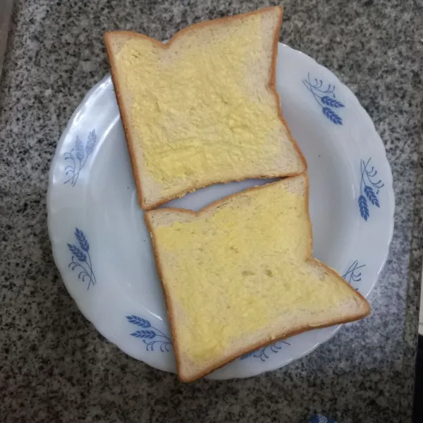 Olesi salah satu bagian roti tawar dengan margarin, ratakan.