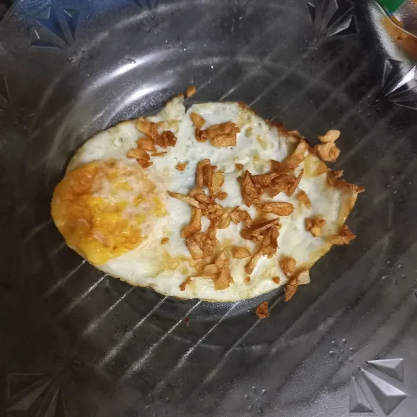 Tuang bawang putih goreng pada telur ceplok.