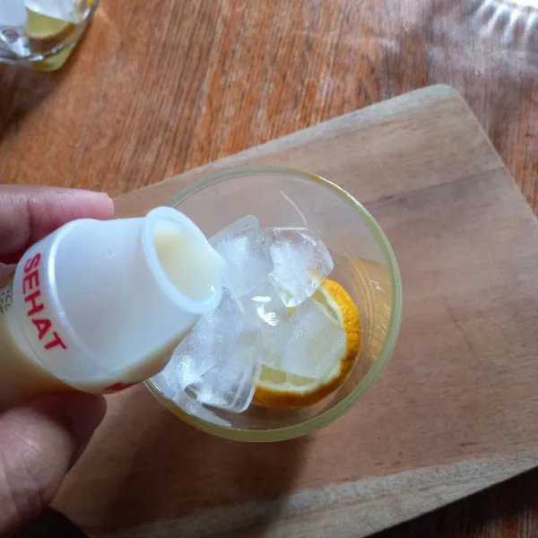 Tuangkan yakult ke dalam gelas yang sudah berisi lemon dan es batu