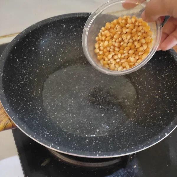 Panaskan minyak dalam wajan. Masukkan jagung popcorn lalu aduk - aduk sampai jagung terbaluri minyak goreng.