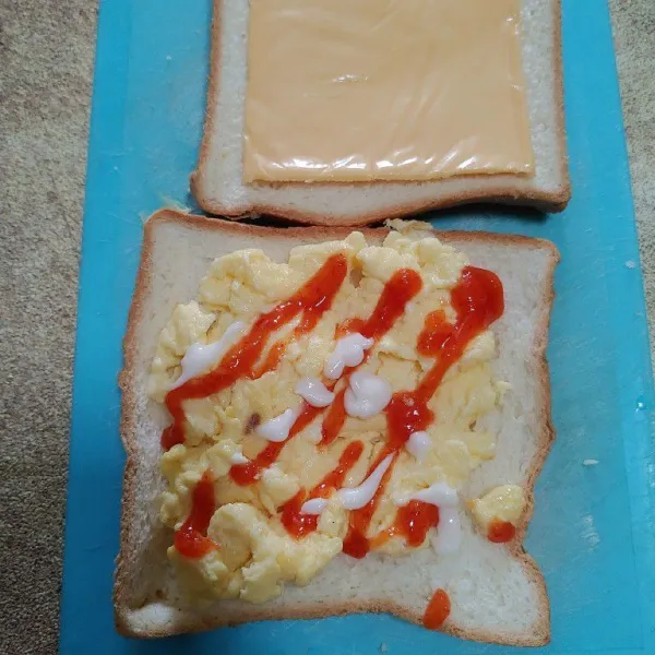 Siapkan 2 lembar roti,tambahkan scramble egg,saos tomat/sambel dan mayonais. Tambahkan keju slice dan tutup dengan roti kembali lalu oles dengan margarin.
