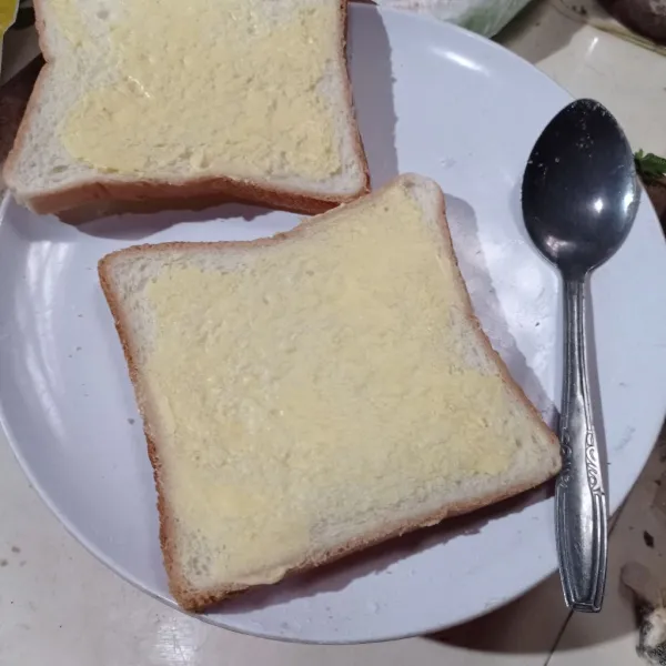 Olesi kedua sisi roti tawar dengan mentega.