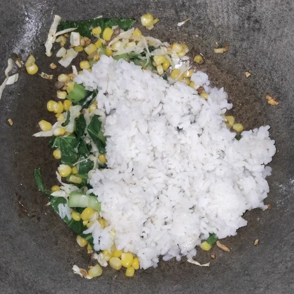 Jika sayuran sudah setengah layu, masukkan dua centong nasi putih ke dalam wajan dan aduk hingga merata.
