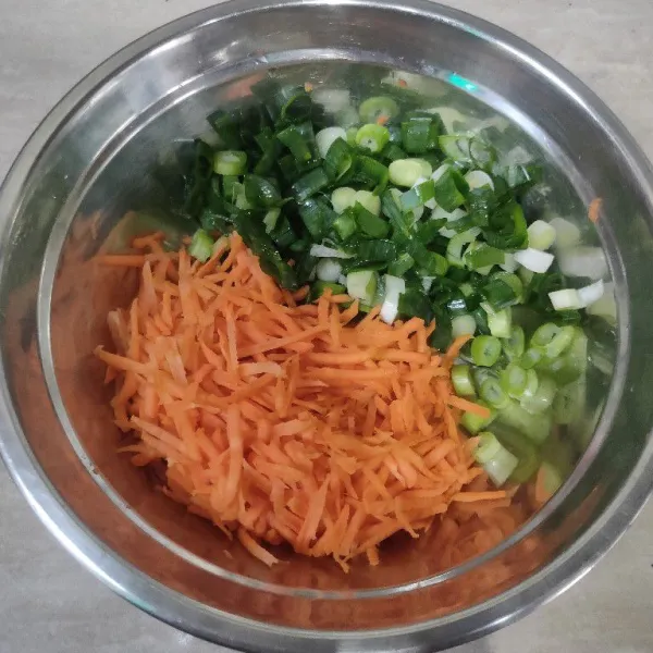 Dalam wadah, siapkan sayuran, wortel dikupas, cuci bersih lalu diparut. Daun bawang dirajang kasar.