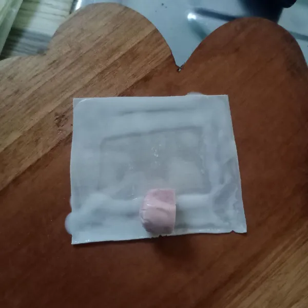 Ambil 1 lembar kulit pangsit. Olesi pinggirannya dengan larutan terigu. Taruh sosis di tengah.