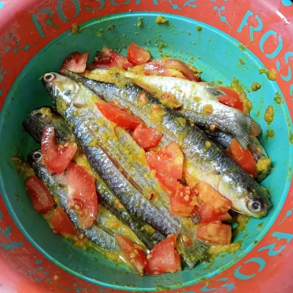 Lumuri ikan dengan bumbu halus, tambahkan juga irisan tomat.