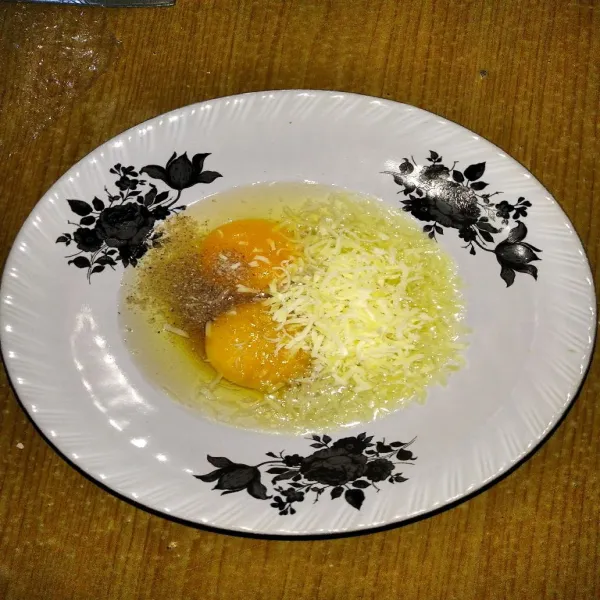Pecahkan 2 butir telur ke dalam mangkok, tambahkan keju, lada, dan kecap ikan.