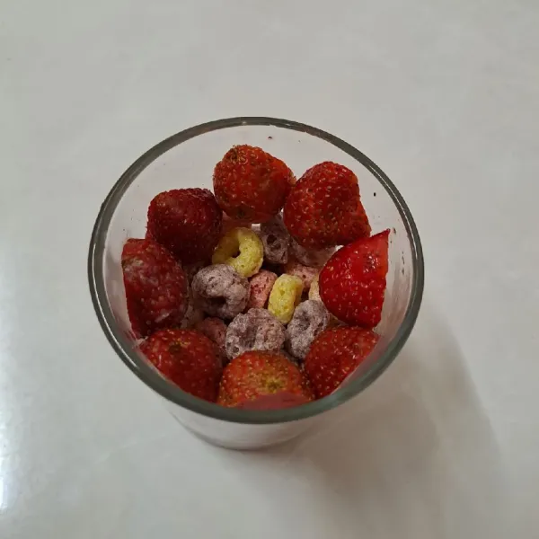 Belah 2 bagian buah strawberry. Kemudian letakkan di dinding gelas sampai penuh.