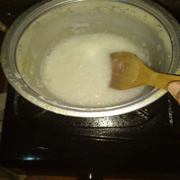 Blender nasi dengan satu siung bawang putih (tidak perlu sampai halus), kemudian masukkan ke dalam panci, tambahkan garam dan kaldu bubuk, masak dengan api kecil hingga bubur mendidih dan mengental.