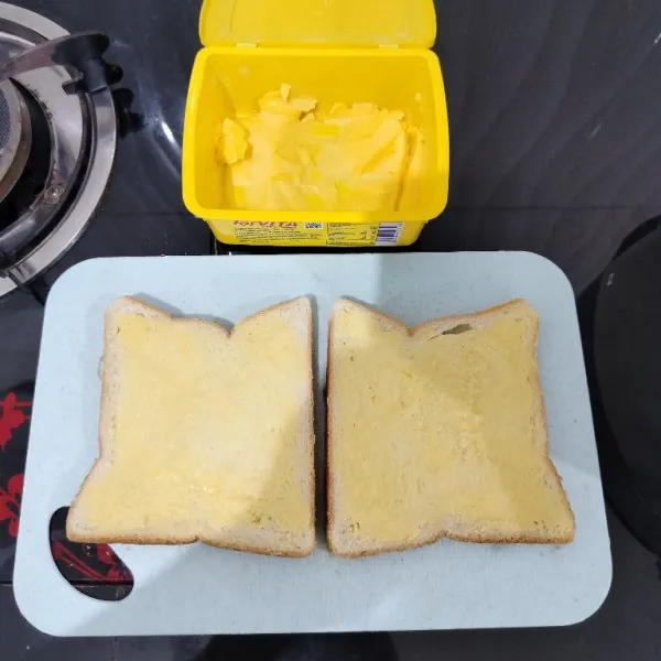 Siapkan roti tawar, lalu olesi salah satu sisi roti dengan margarin.