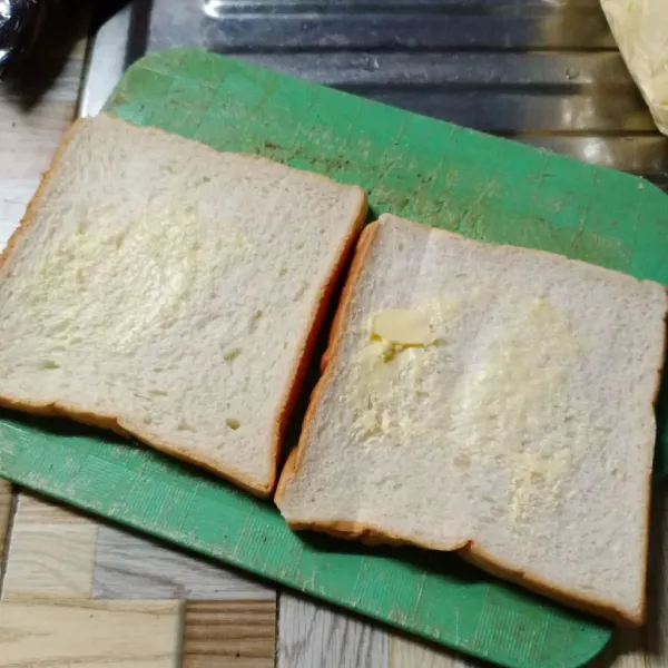 Oles permukaan roti tawar dengan margarin.