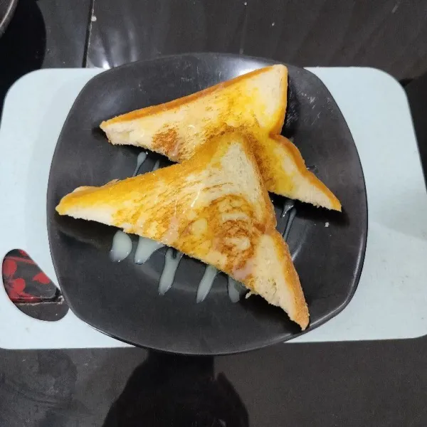 Potong roti menjadi bentuk segitiga. Lalu tata di piring dan beri topping krimer kental manis.