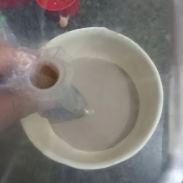 Tuang susu cair dengan bantuan corong ke dalam plastik.