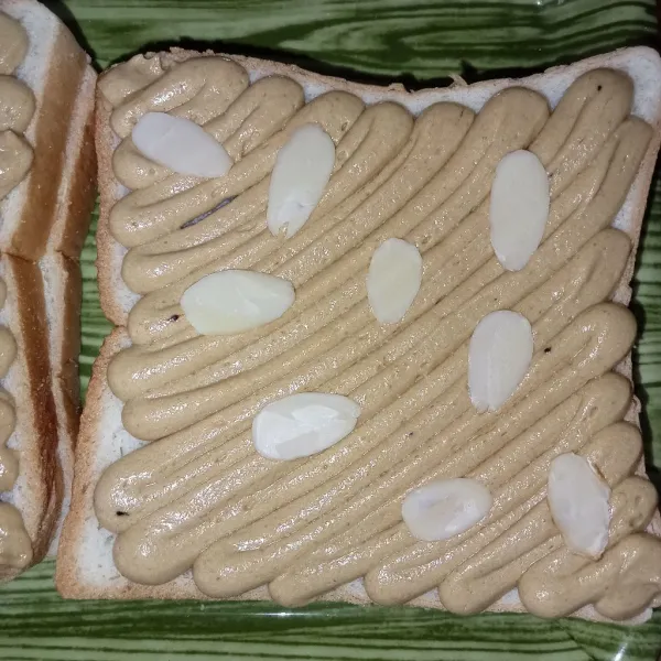 Semprotkan adonan topping di atas roti, kemudian letakkan almond slices di atasnya.