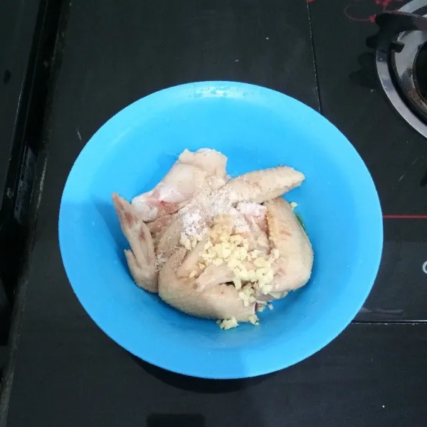 Masukkan sayap ayam ke dalam mangkuk. Tambahkan bawang putih, merica bubuk, dan garam. Aduk rata.