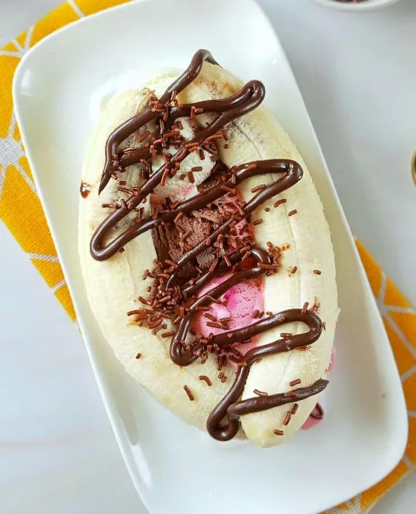 Tata pisang di samping kanan dan kiri ice cream lalu tambahkan cokelat topping di atasnya dan tambahkan taburan meises.