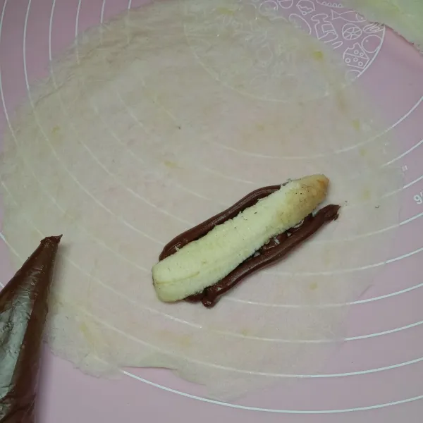 Siapkan satu lembar kulit lumpia, beri selai cokelat, lalu potongan pisang. Gulung bagian bawahnya satu kali. Lalu lipat sisi kiri kanannya.
