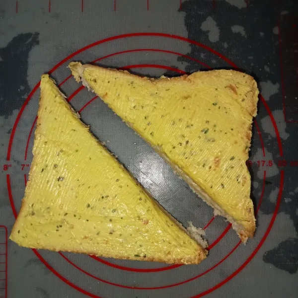 Olesi bagian luar atas dan bawah roti dengan garlic butter kemudian potong menjadi dua berbentuk segitiga.
