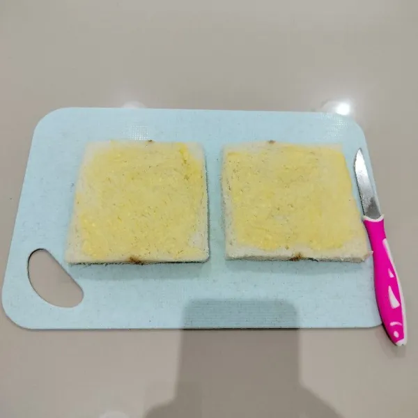 Siapkan roti tawar, lalu oles sisi dalamnya dengan margarin.
