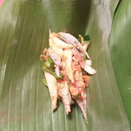 Selanjutnya siapkan daun pisang, panggang sebentar di atas api kompor agar layu tidak mudah robek. Ambil secukupnya adonan ikan dan bumbu tadi, taruh di atas daun pisang. Kemudian bungkus, semat dengan lidi.