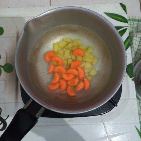Didihkan air, masukkan kentang dan wortel rebus sampai setengah matang.
