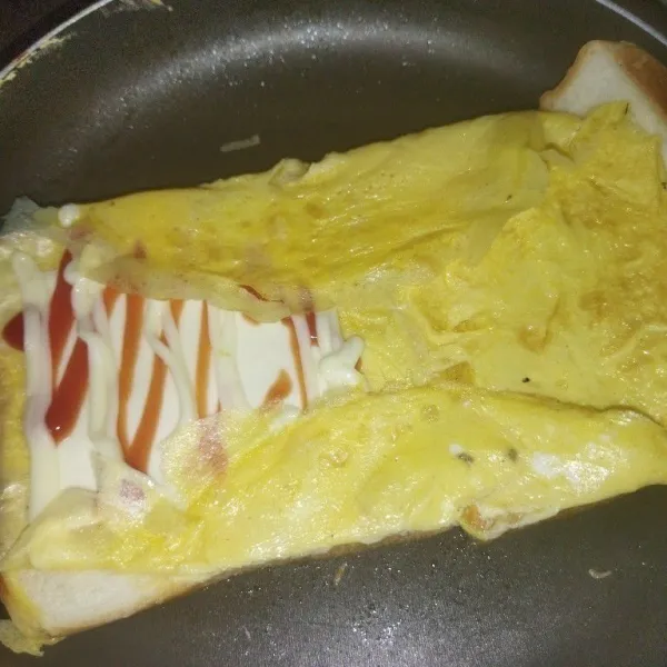 Tata 1 lembar keju cheddar, mayones dan saus, sambal, lalu lipay telurnya ke atas roti.