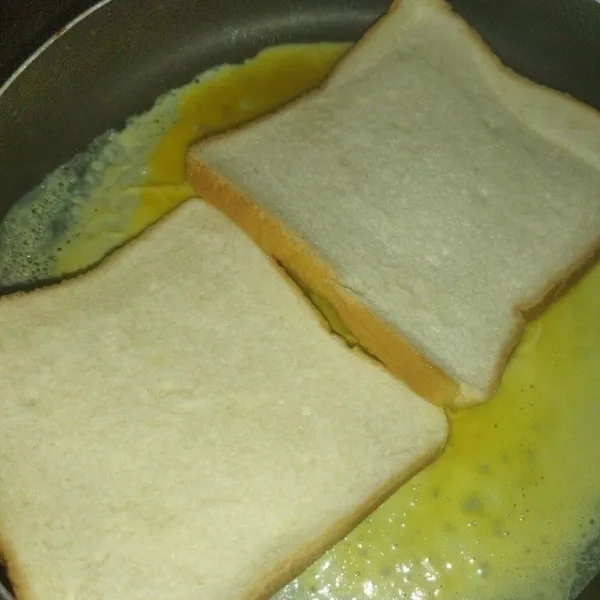 Panaskan wajan, oleh wajan dengan margarin, lalu kecilkan api kompor, lalu tuang telur, tata 2 lembar roti tawar diatas permukaan telur yang masih berair.