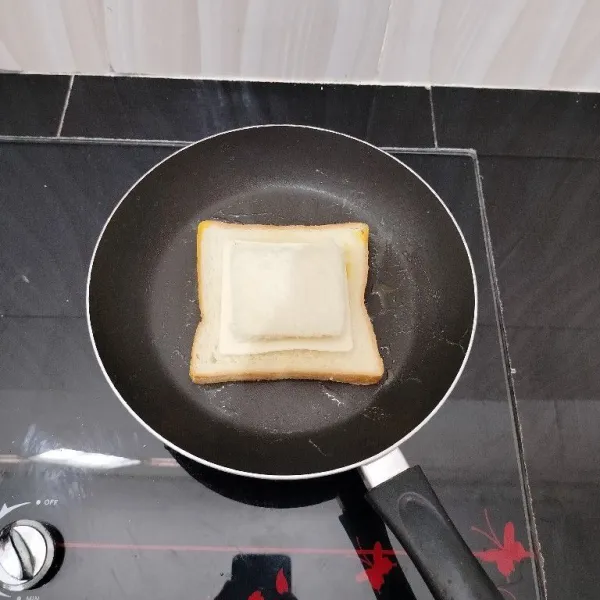 Kemudian beri keju slices di atas telur. Lalu beri potongan roti diatasnya. Masak hingga bagian bawah roti matang.