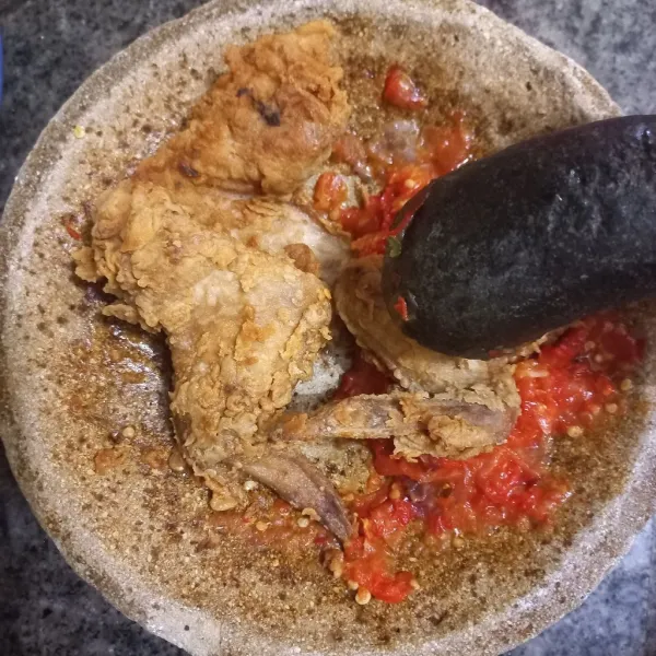 Masukkan ayam goreng pada cobek, lalu geprek ayam dan lumuri dengan sambalnya.