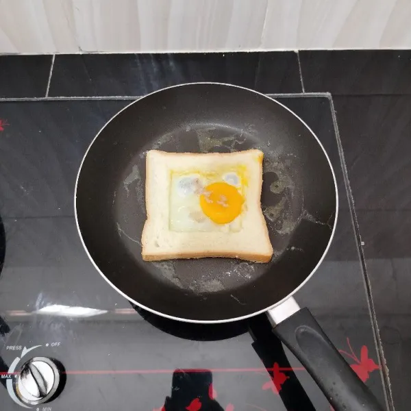 Lalu masukkan roti tawar. Kemudian ceplok telur di lubang tengahnya. Taburi dengan merica bubuk.