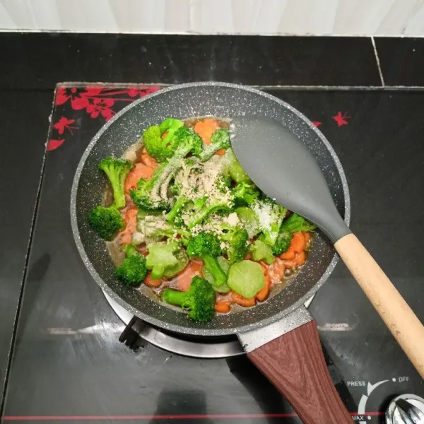 Masukkan brokoli, merica bubuk, kaldu jamur, dan garam. Aduk rata, masak hingga brokoli setengah layu.