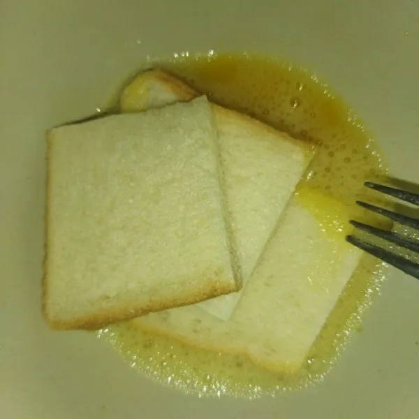 Potong roti tawar menjadi 4 bagian, lalu celupkan ke dalam telur.