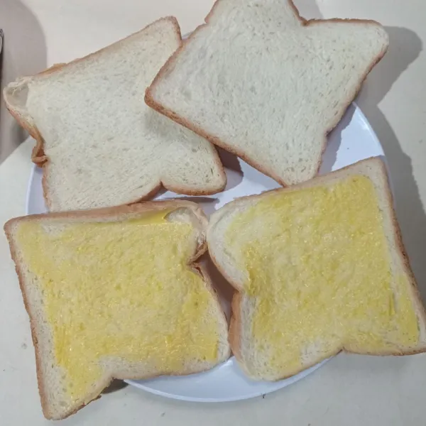 Olesi 2 bagian roti tawar dengan margarin.