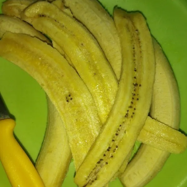 Panaskan minyak goreng, kupas pisang tanduk, lalu potong memanjang 1 pisang menjadi 4 bagian.