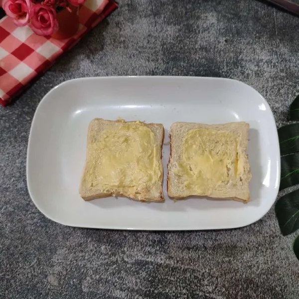 Oles permukaan roti tawar dengan margarin.