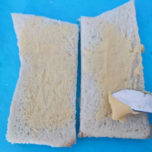 Buang pinggiran roti tawar, potong jadi 2. Kemudian oles dengan margarin.