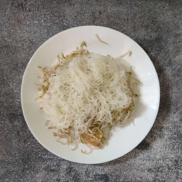 Tata tahu yang sudah dipotong-potong ke atas piring saji, lalu beri taoge dan bihun.