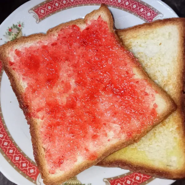 Oles roti dengan selai strawberry, tangkupkan roti dan siap disajikan.