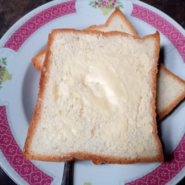 Oles permukaan roti dengan margarin.