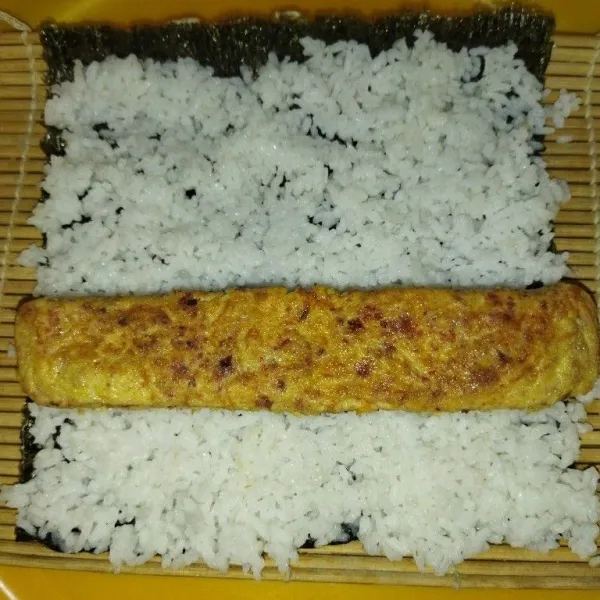 Tata nori sushi lalu tata nasi diatas nori, kemudian taruh tamagoyaki lalu gulung sambil ditekan perlahan.