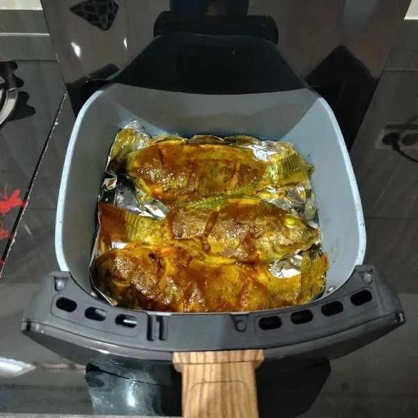 Tata ikan mujair di dalam air fryer. Olesi dengan bumbu olesan. Bakar hingga sisi atas matang.